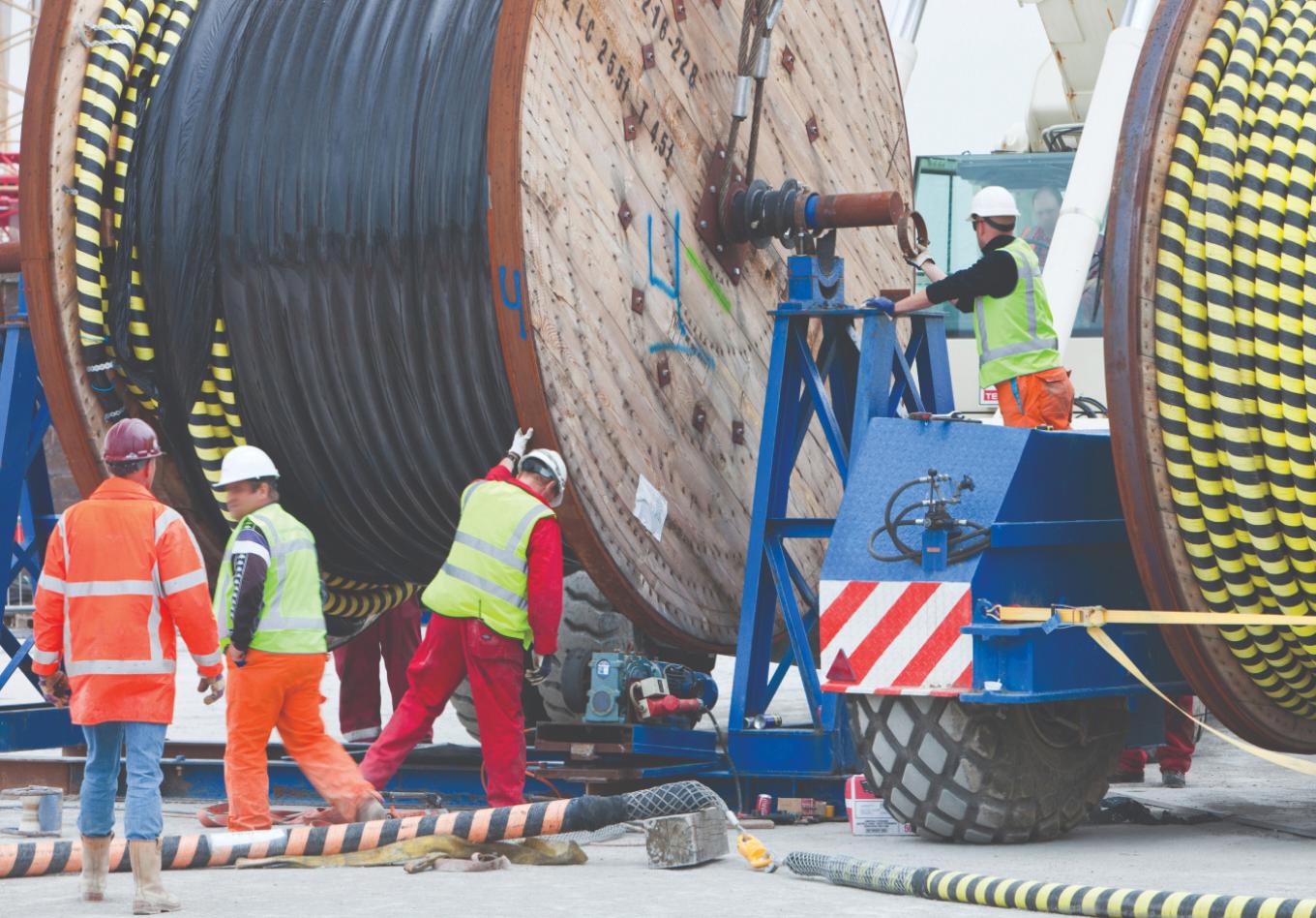 Workers loading cable drums onto a drum stand