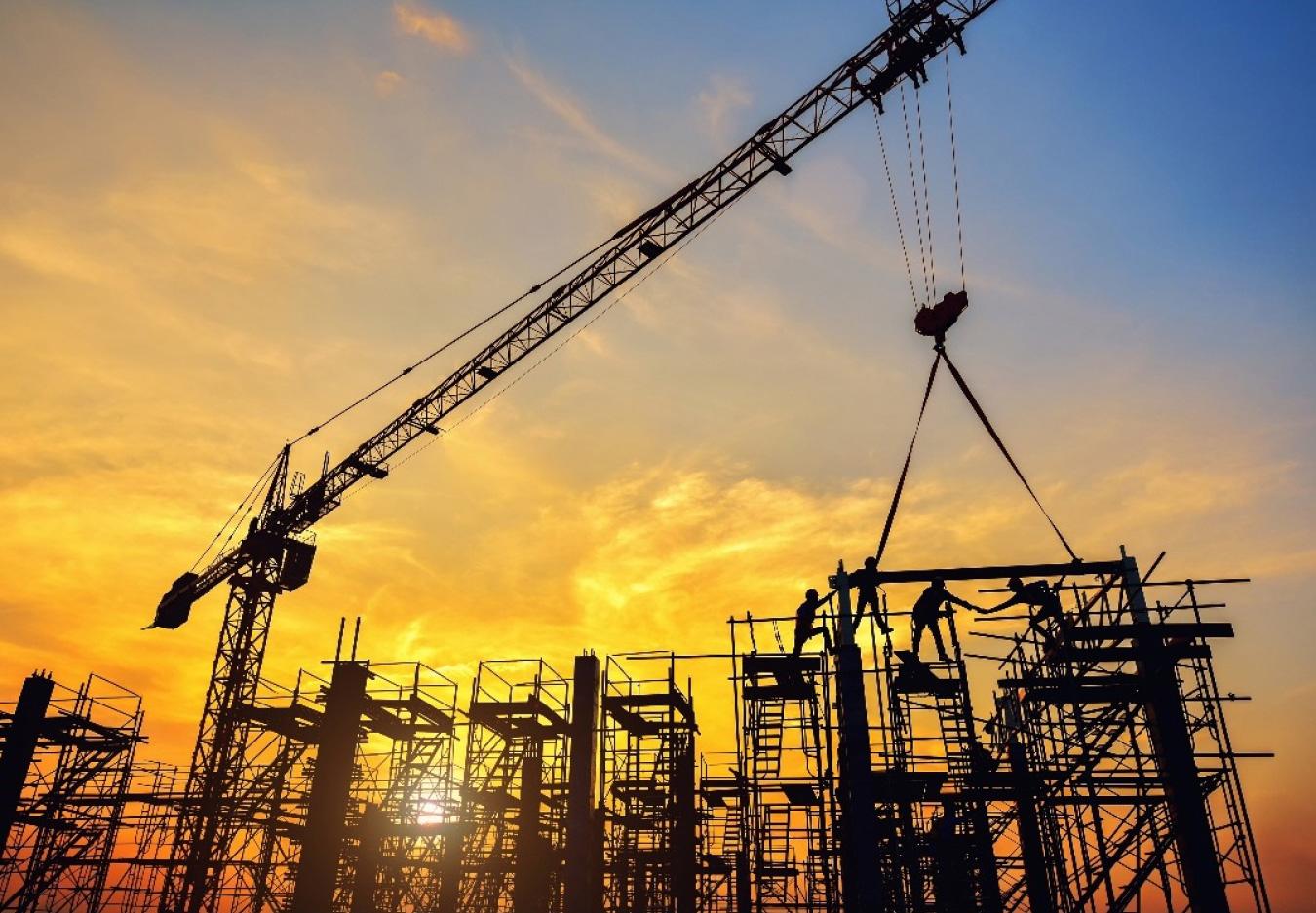 Tower crane and construction workers silhouetted at sunset
